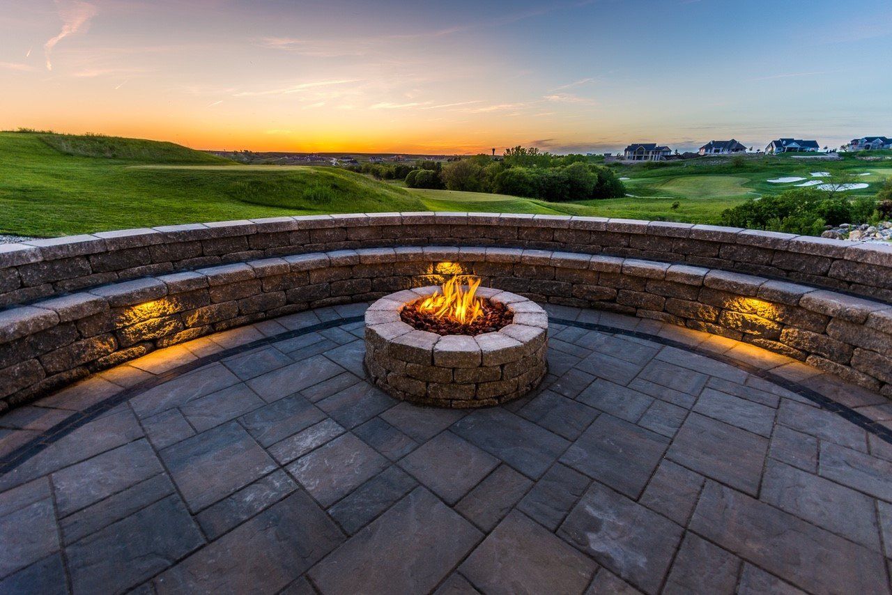 A fire pit on a patio with a view of a golf course at sunset.
