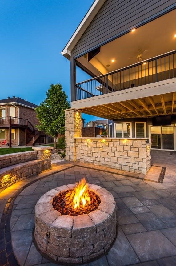A fire pit is in the middle of a patio in front of a house.