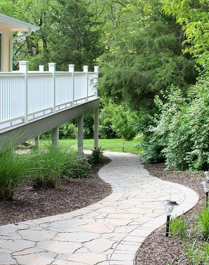 A walkway leading to a house with a white deck surrounded by trees.