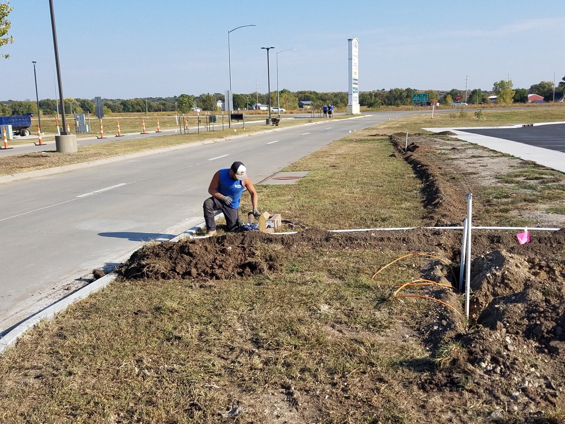 A man is kneeling in the dirt next to a road.