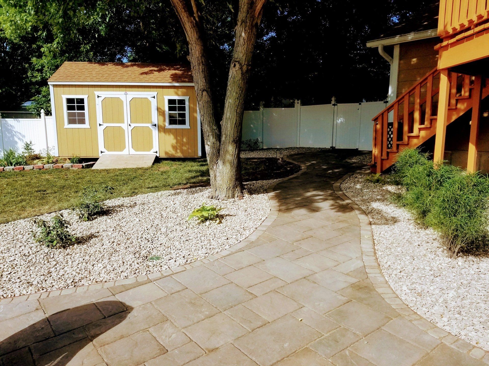 A yellow shed is in the backyard next to a stone walkway.