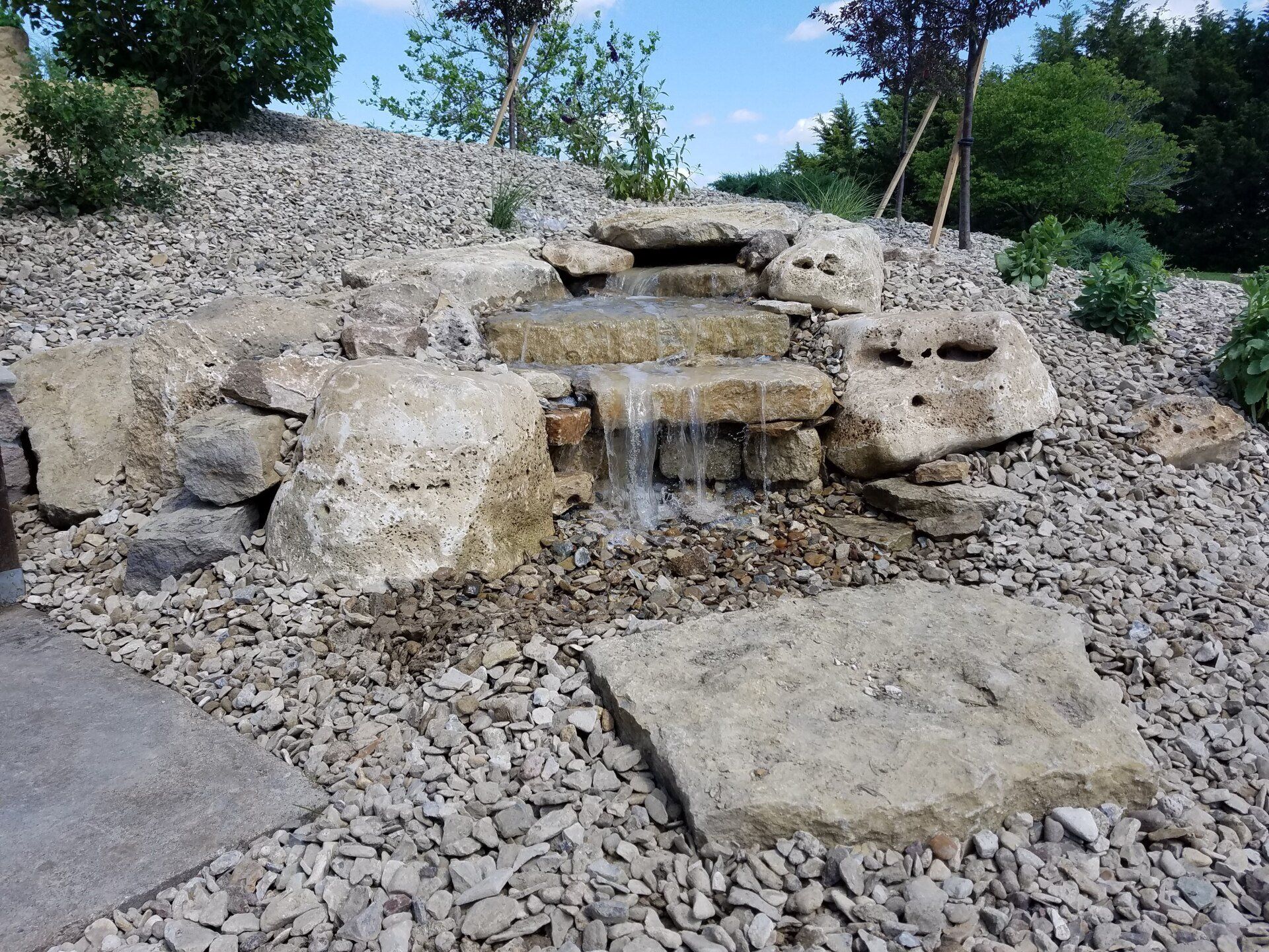 A small waterfall is surrounded by rocks and gravel.