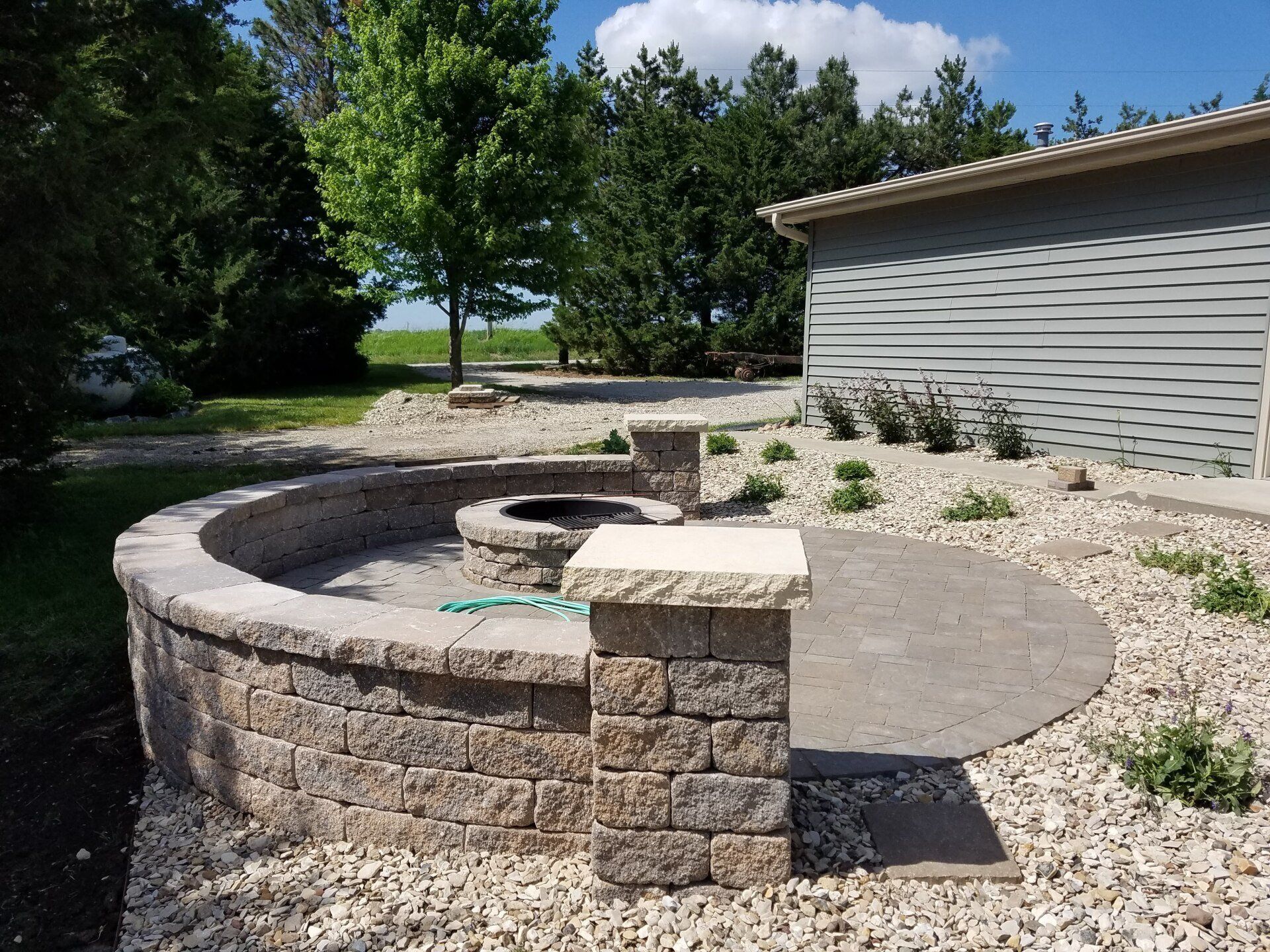 A fire pit is surrounded by a stone wall and gravel in front of a house.