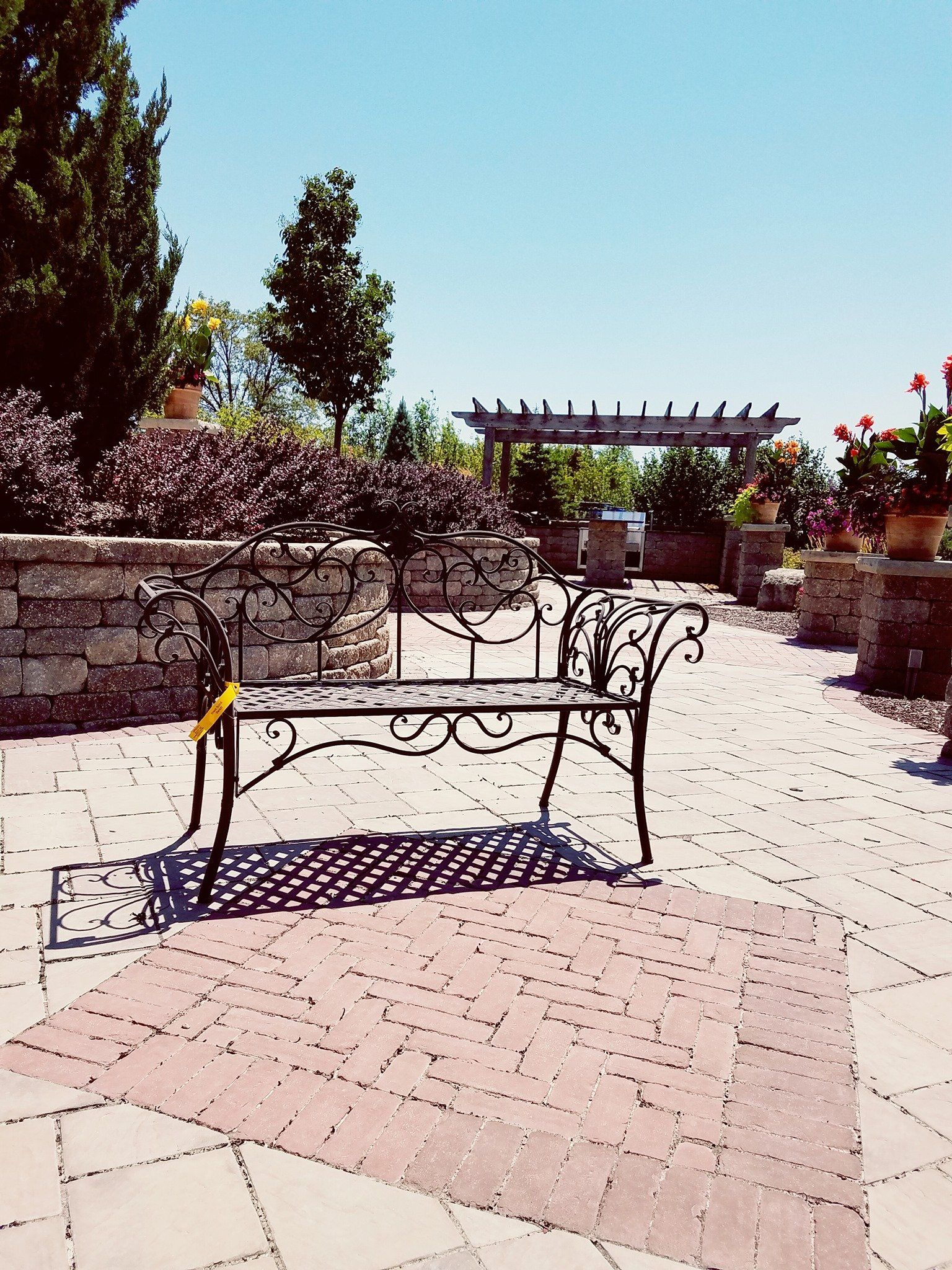 A wrought iron bench sits on a brick walkway