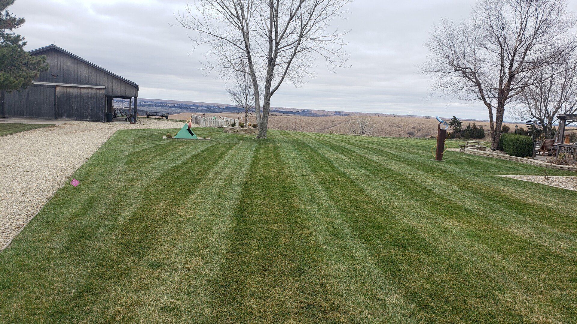 A lush green lawn with a gravel driveway and a barn in the background.