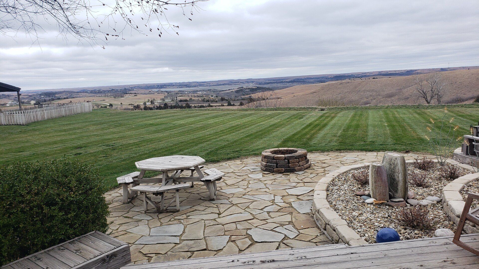 A patio with a picnic table and benches and a fire pit in the middle of a lush green field.
