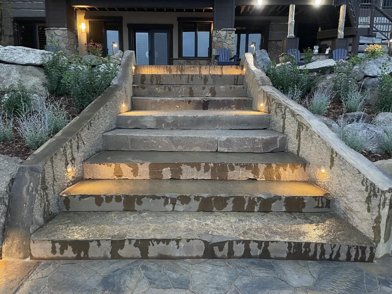 Concrete front steps with wet patches leading up to a dark building entrance, flanked by stone walls and landscaping