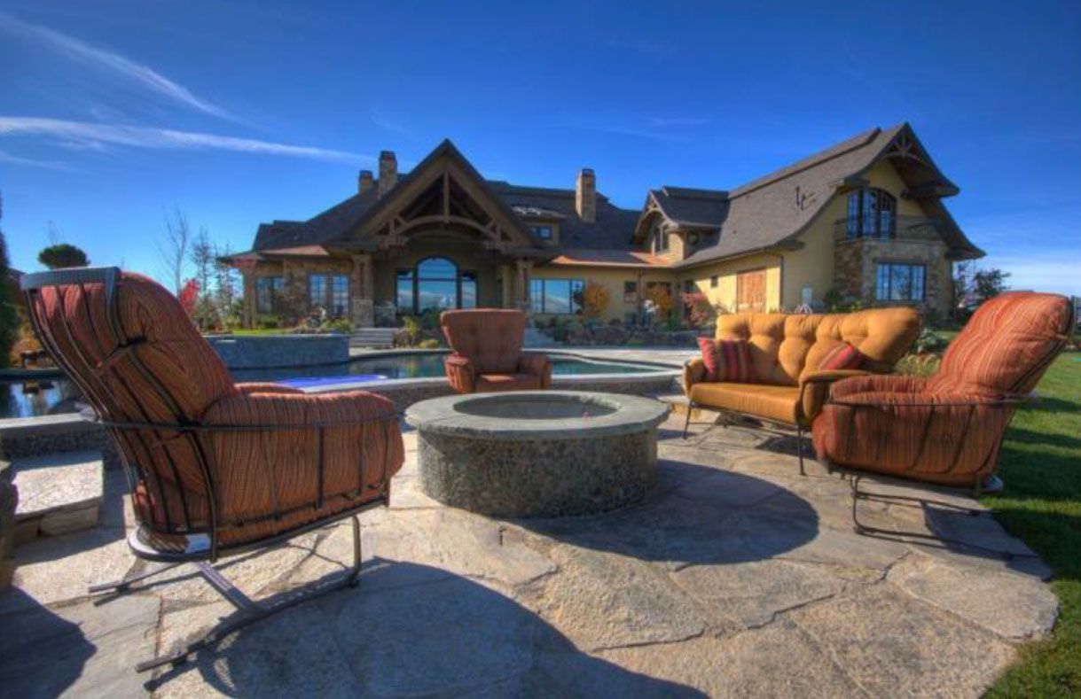 Patio seating around a fire pit in front of a large house with a blue sky.