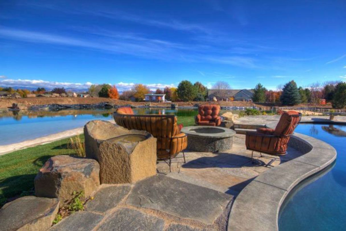 Patio with stone seating, fire pit, and pool; blue sky and distant houses.