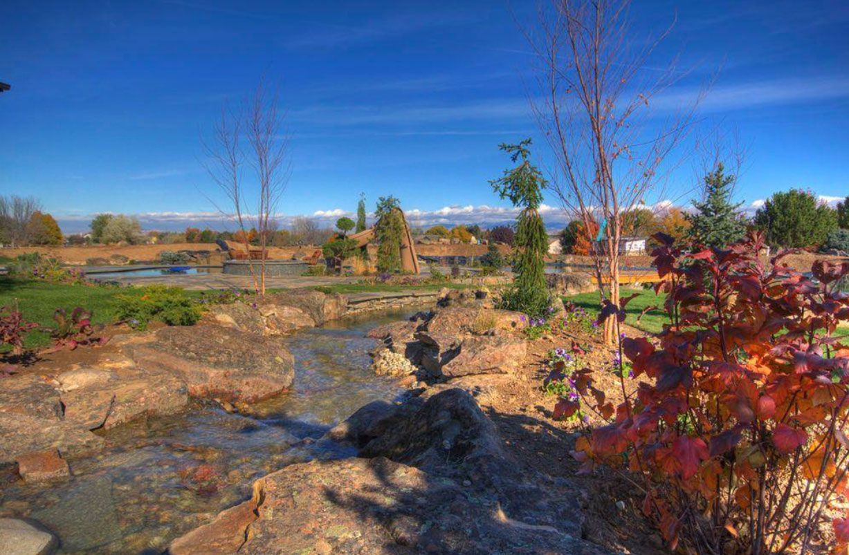 A stream flows through a landscaped park with rocks, trees, and a clear blue sky.