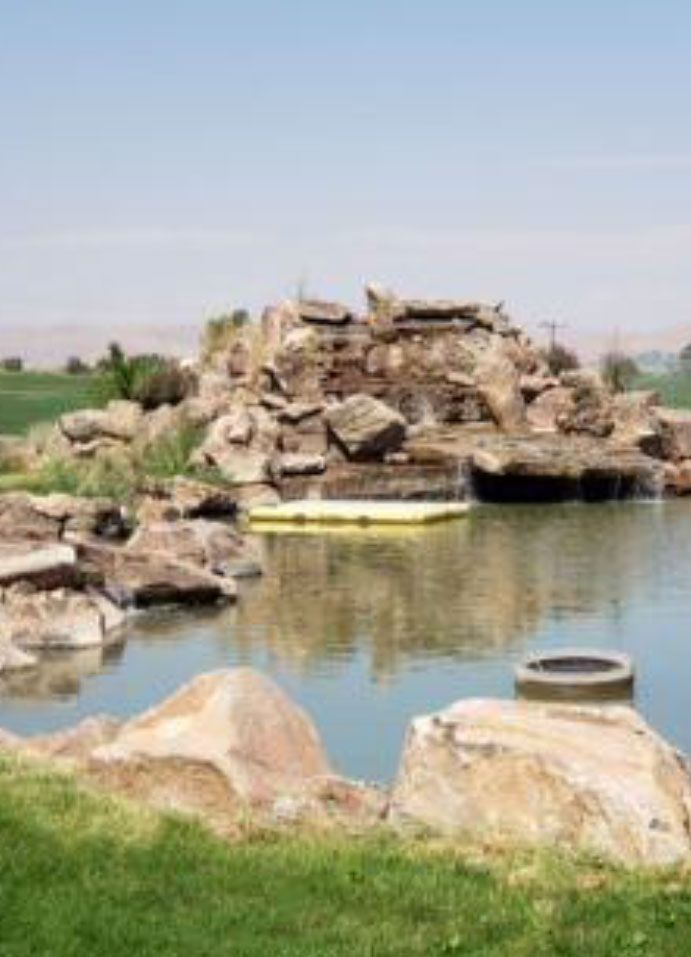 Water feature with a rocky waterfall and pond, on a golf course under a clear sky.