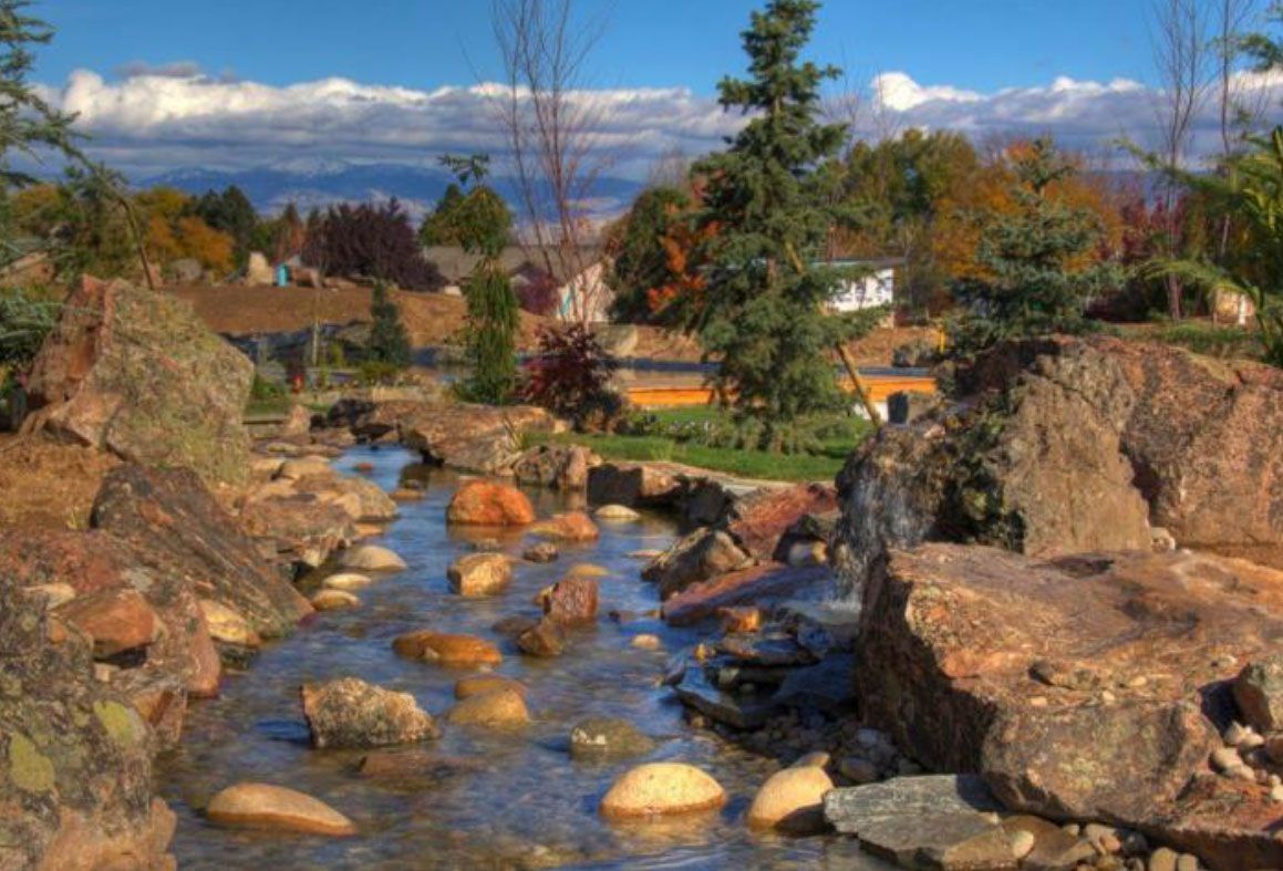 A stream with water flowing over rocks. Trees with colorful leaves in the background under a blue sky.