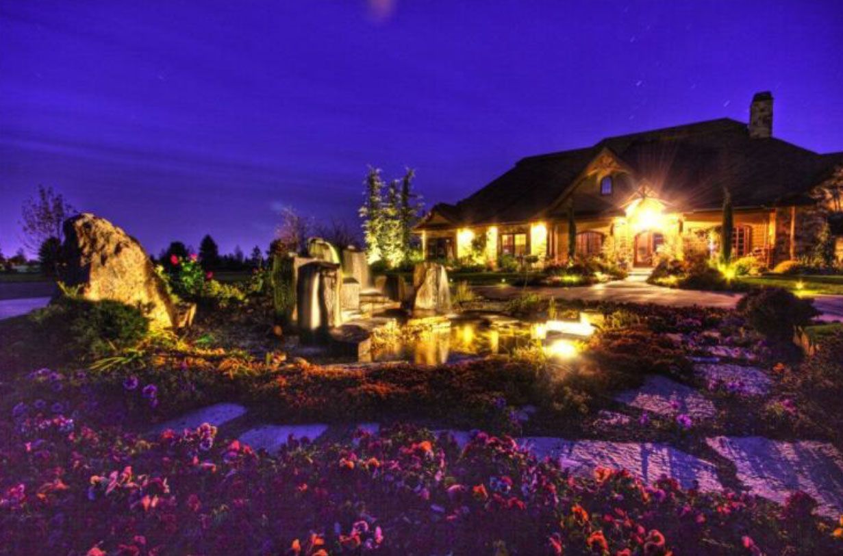 Illuminated house at night with a pond and landscaping under a dark blue sky.