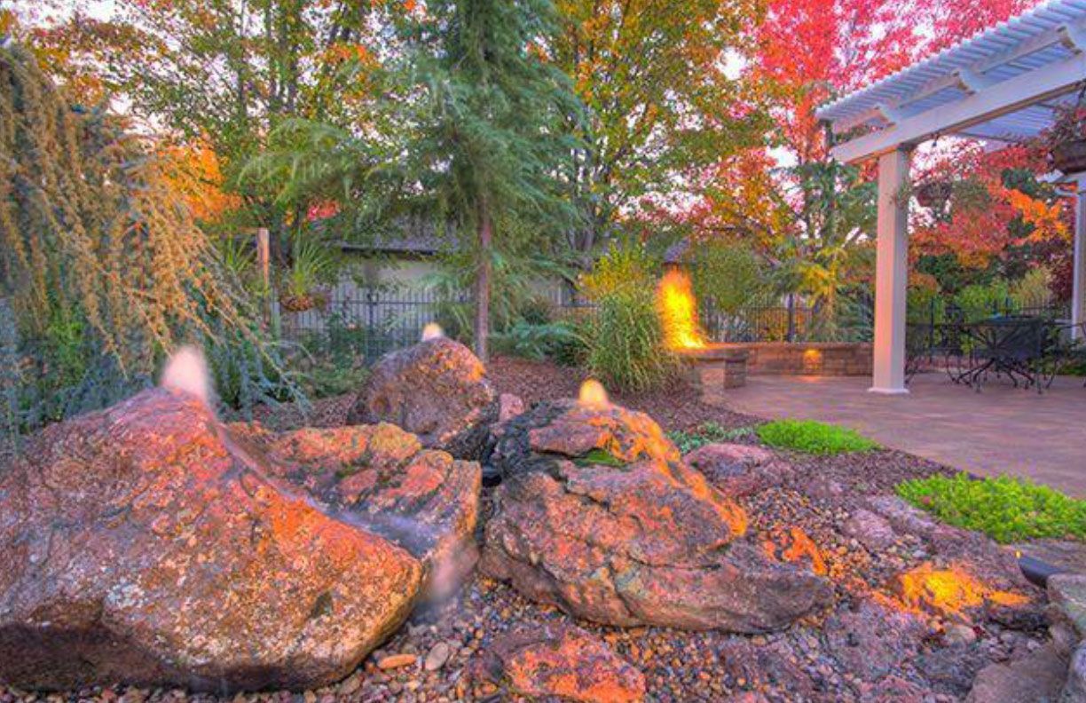 Rocks with water features in a garden; trees and patio with fire pit visible.
