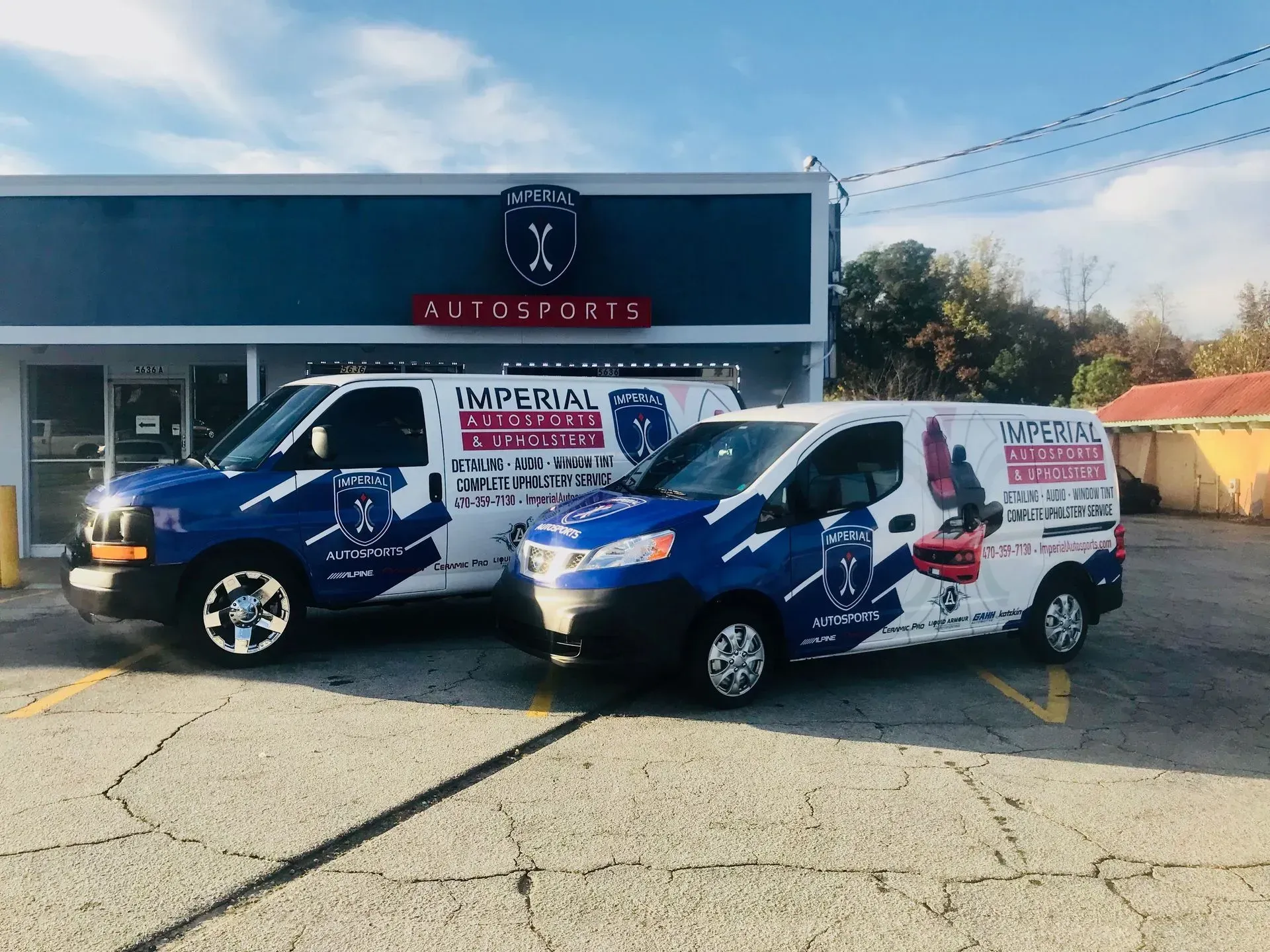 Two blue and white Imperial vans parked in front of a building with a blue facade and a sign that reads