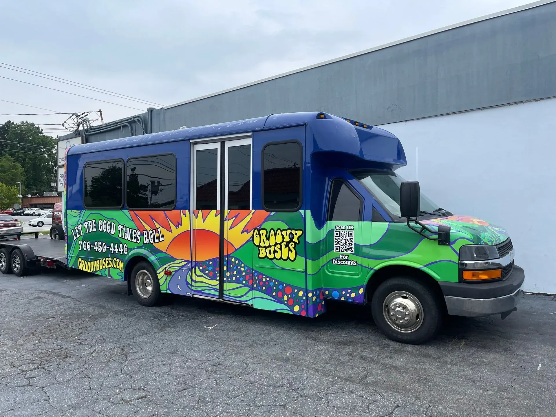 Colorful bus with mural art parked outside a building, towing a trailer.