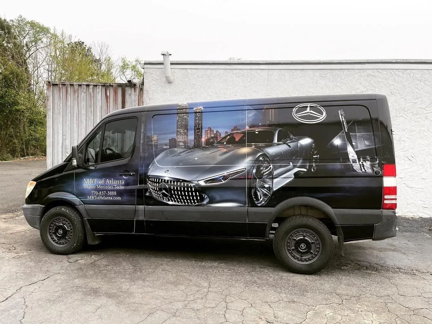 Black Mercedes Sprinter van with car and city graphic wrap.