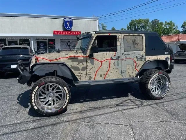 Customized Jeep Wrangler with camouflage wrap, oversized chrome wheels, parked in front of a building.