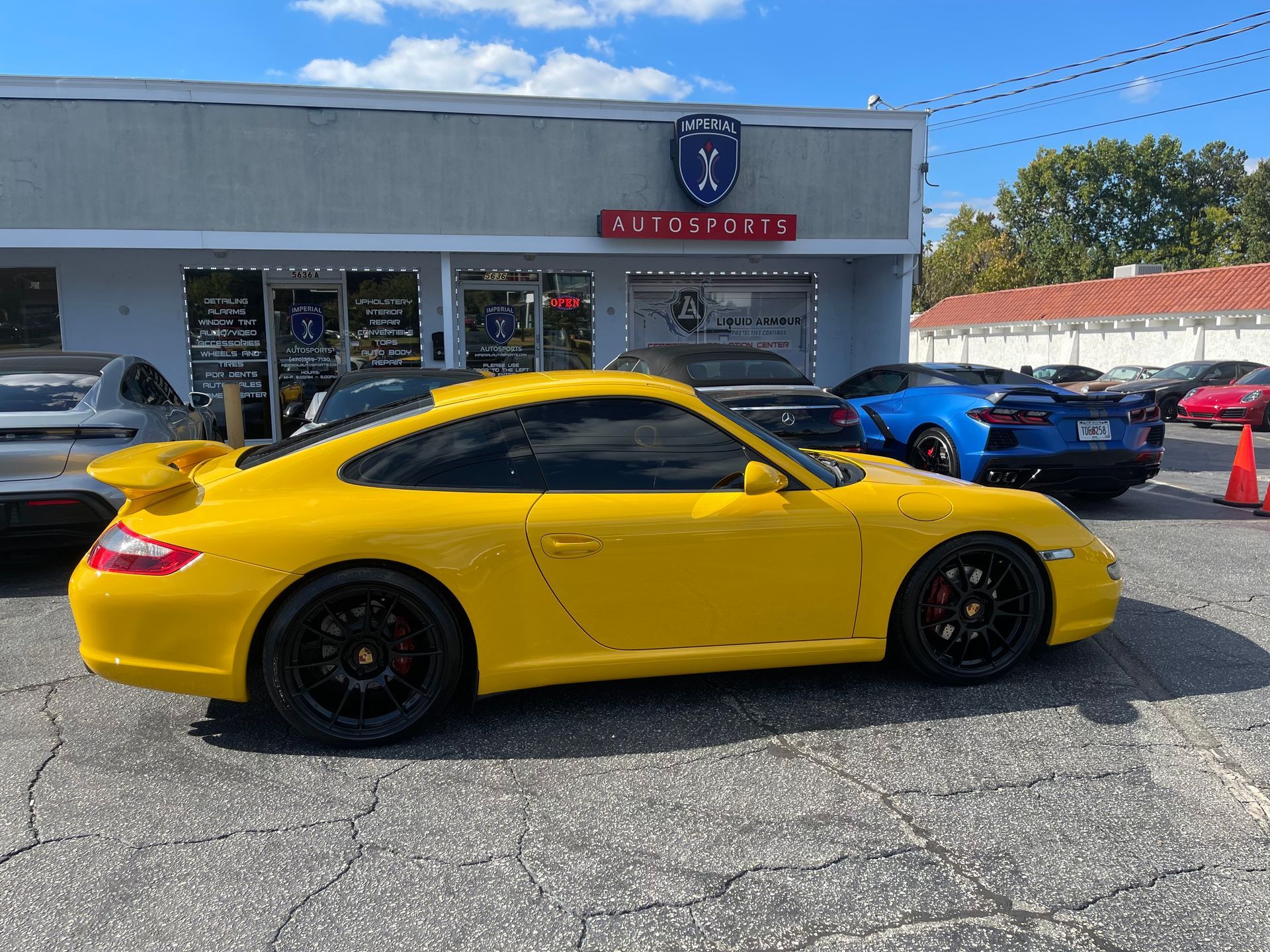 A yellow Porsche 911 is parked in front of a car dealership.