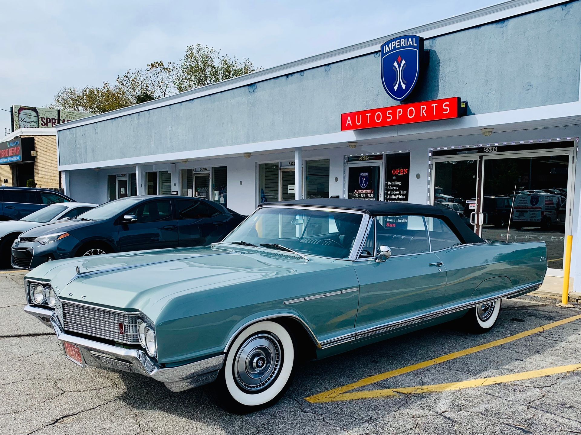 A classic car is parked in front of a car dealership.