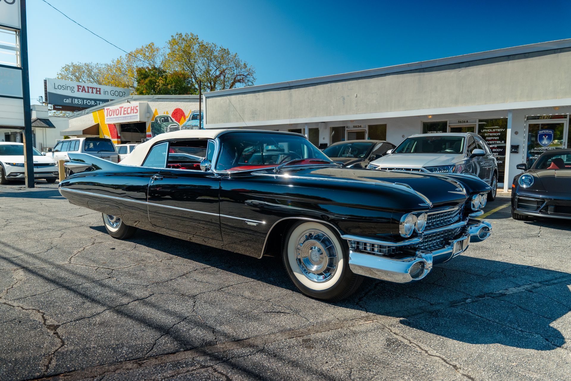 A black Cadillac is parked in front of a car dealership.