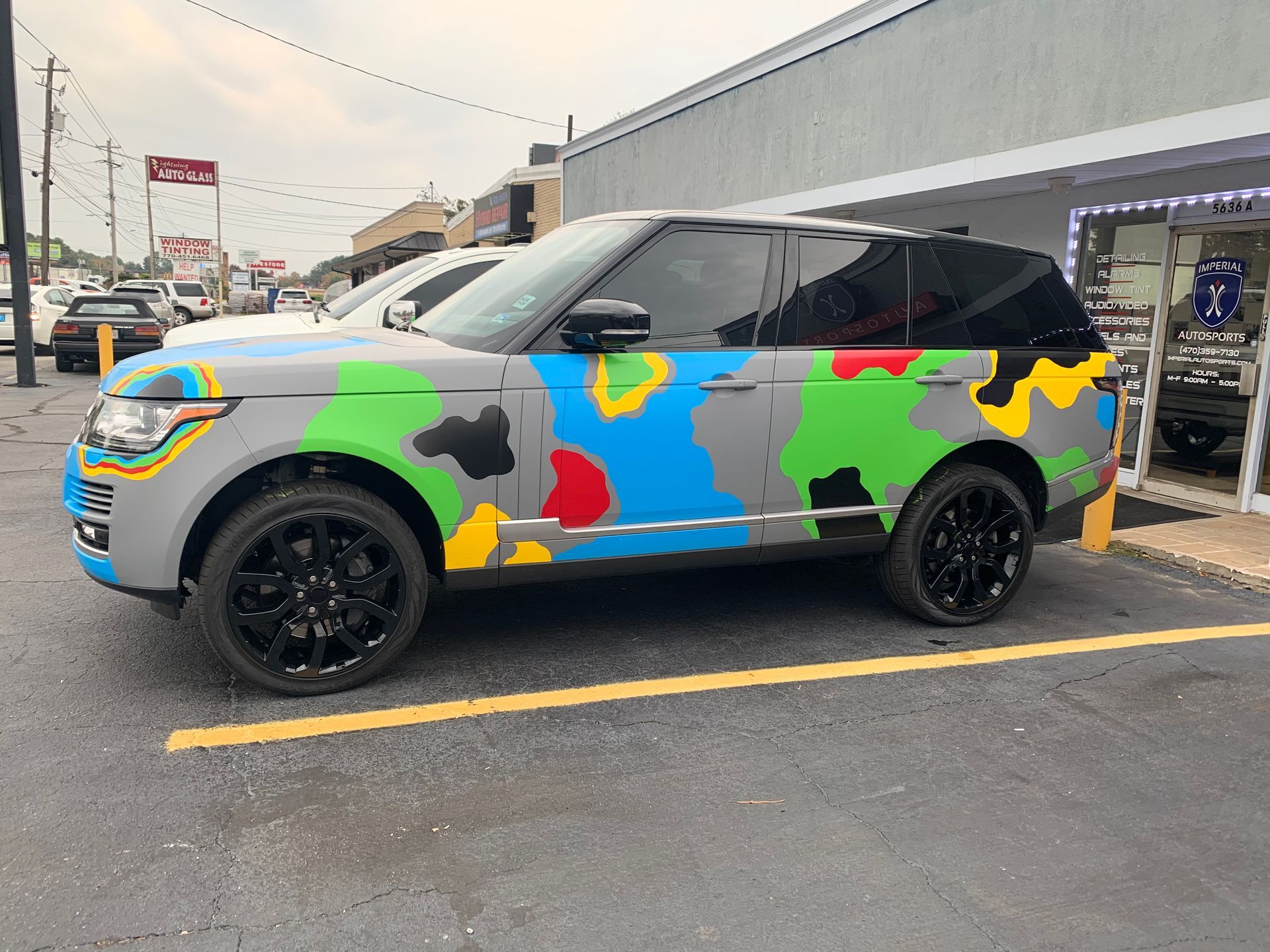 A Range Rover wrapped in camouflage paint is parked in a parking lot.