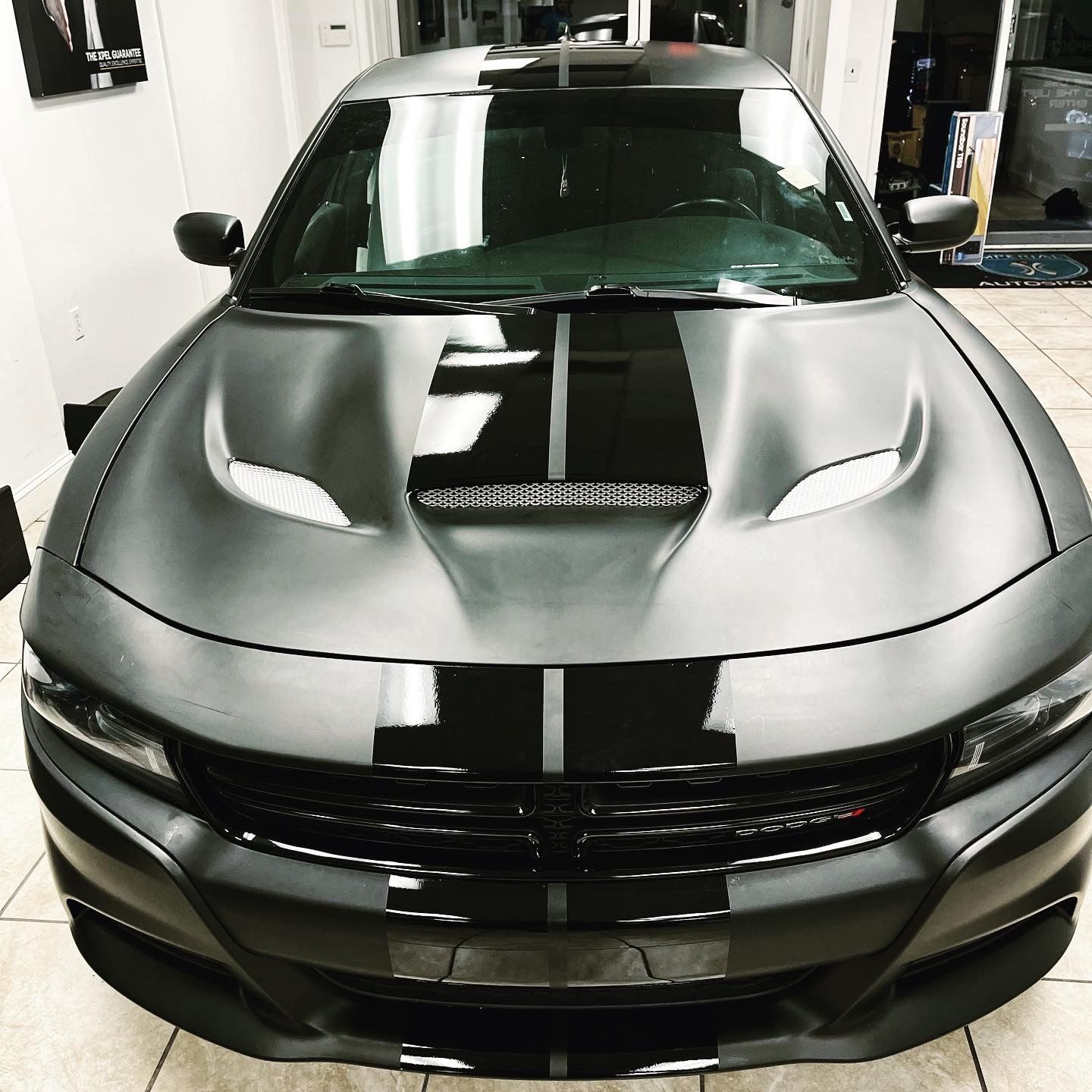 A gray Dodge Charger with black stripes on the hood
