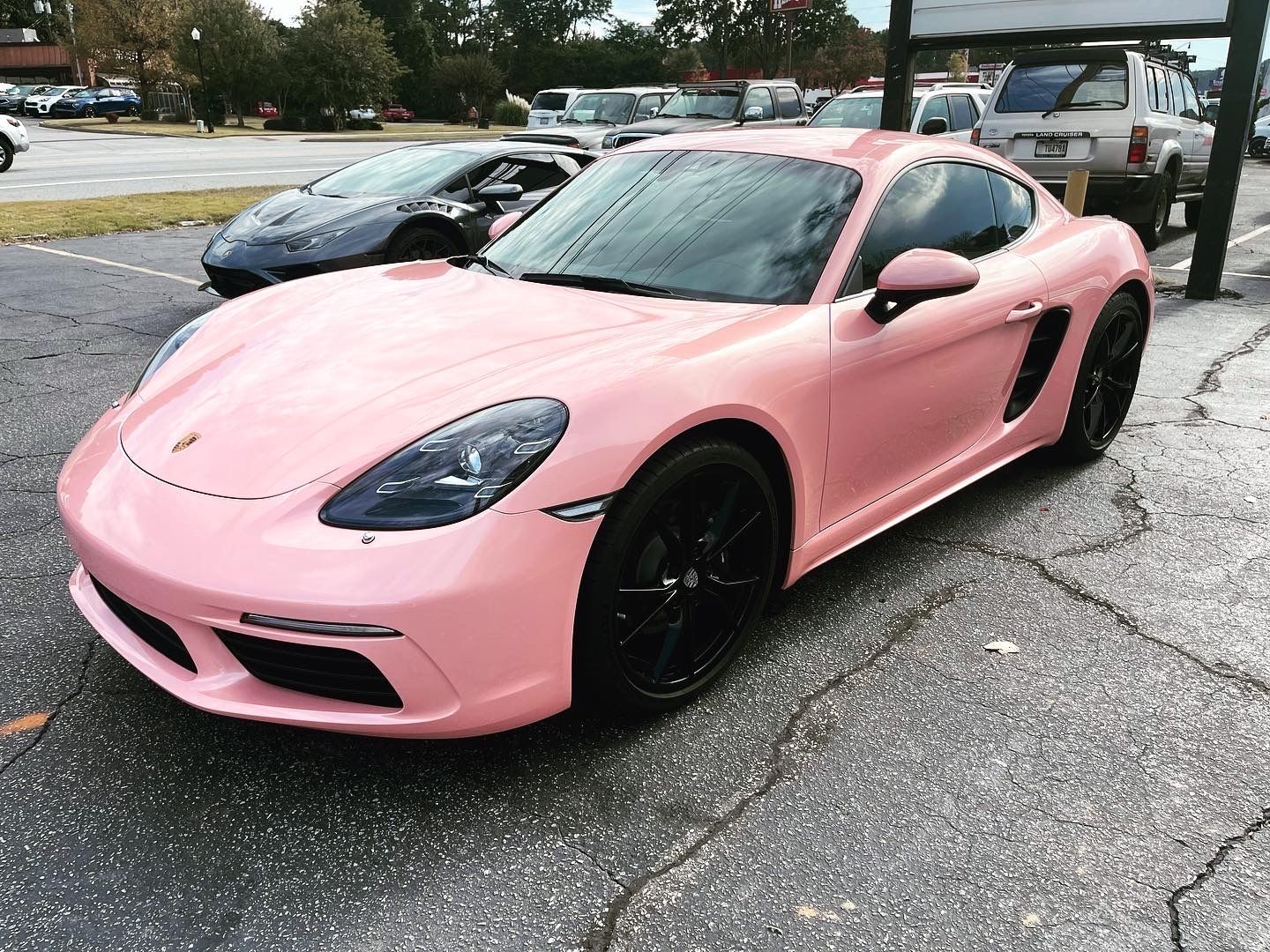 A pink Porsche is parked in a parking lot