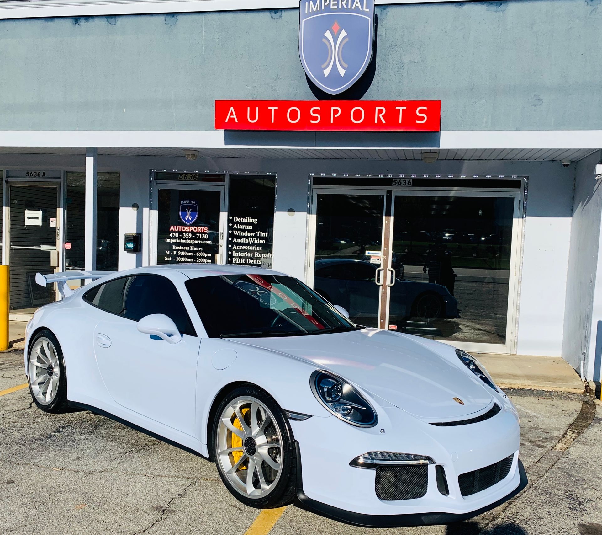 A white Porsche 911 GT3 RS is parked in front of a car dealership.