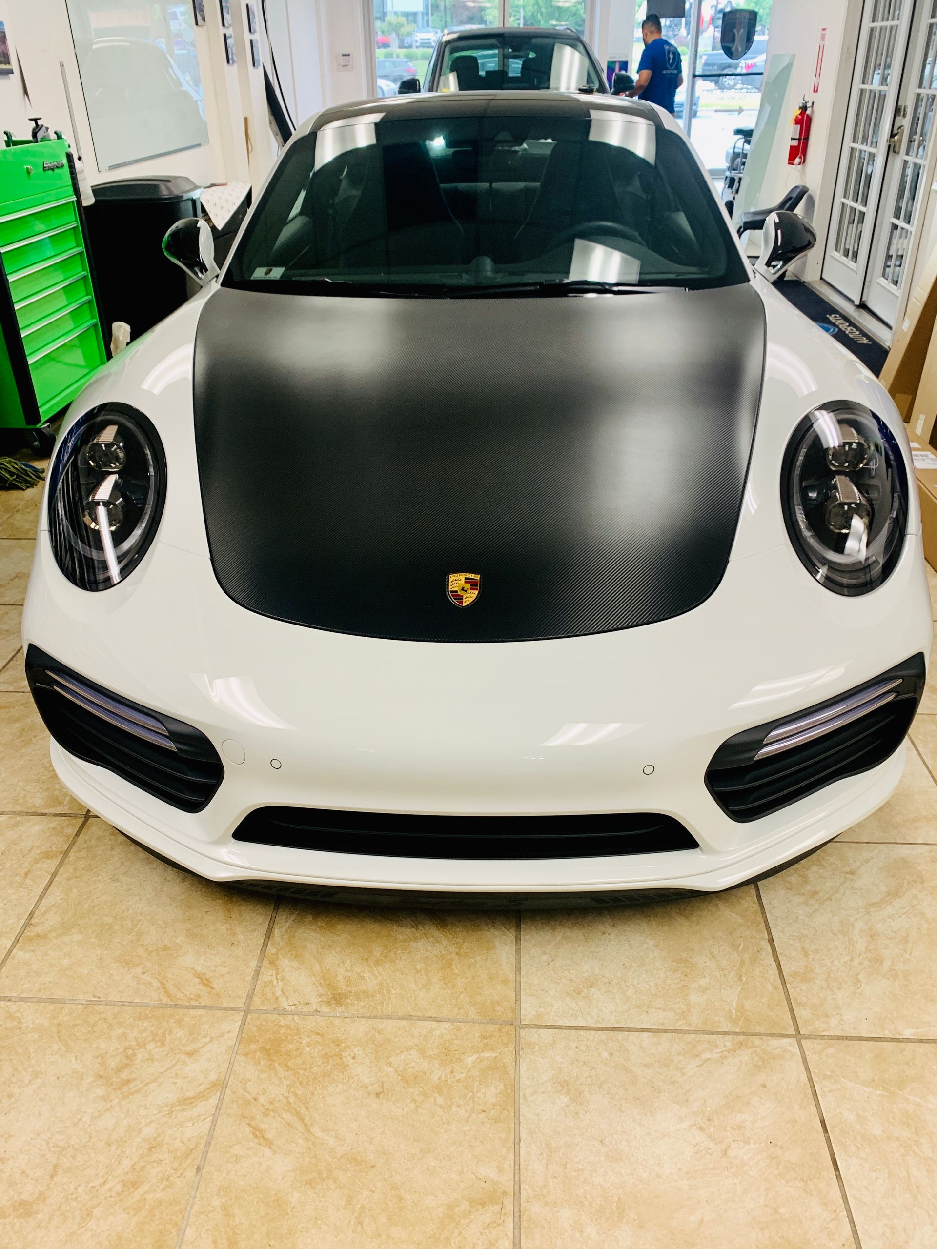 A white sports car with a black hood is parked in a garage.
