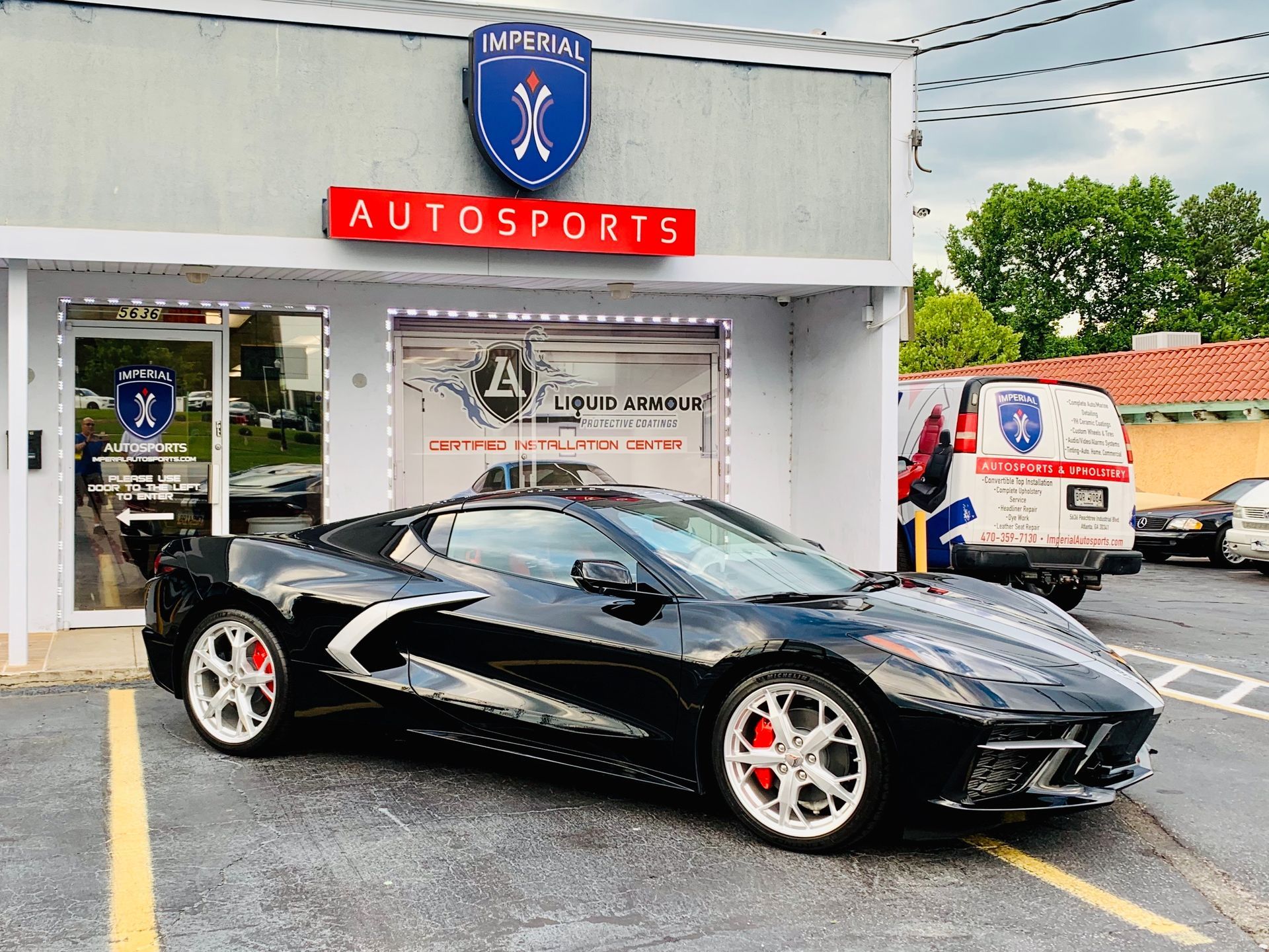 A black sports car is parked in front of a car dealership.