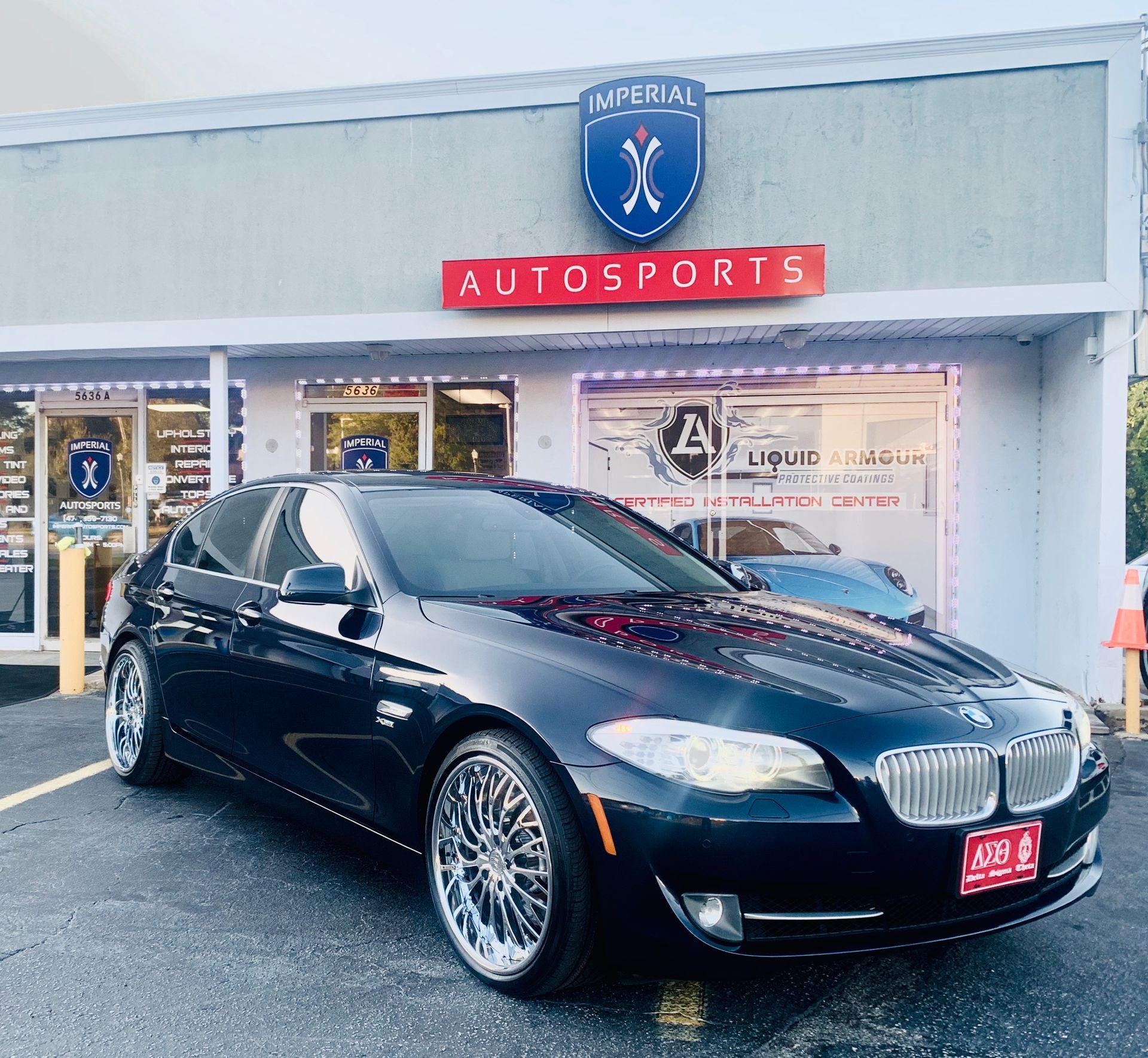 A black car is parked in front of a building that says Autosports