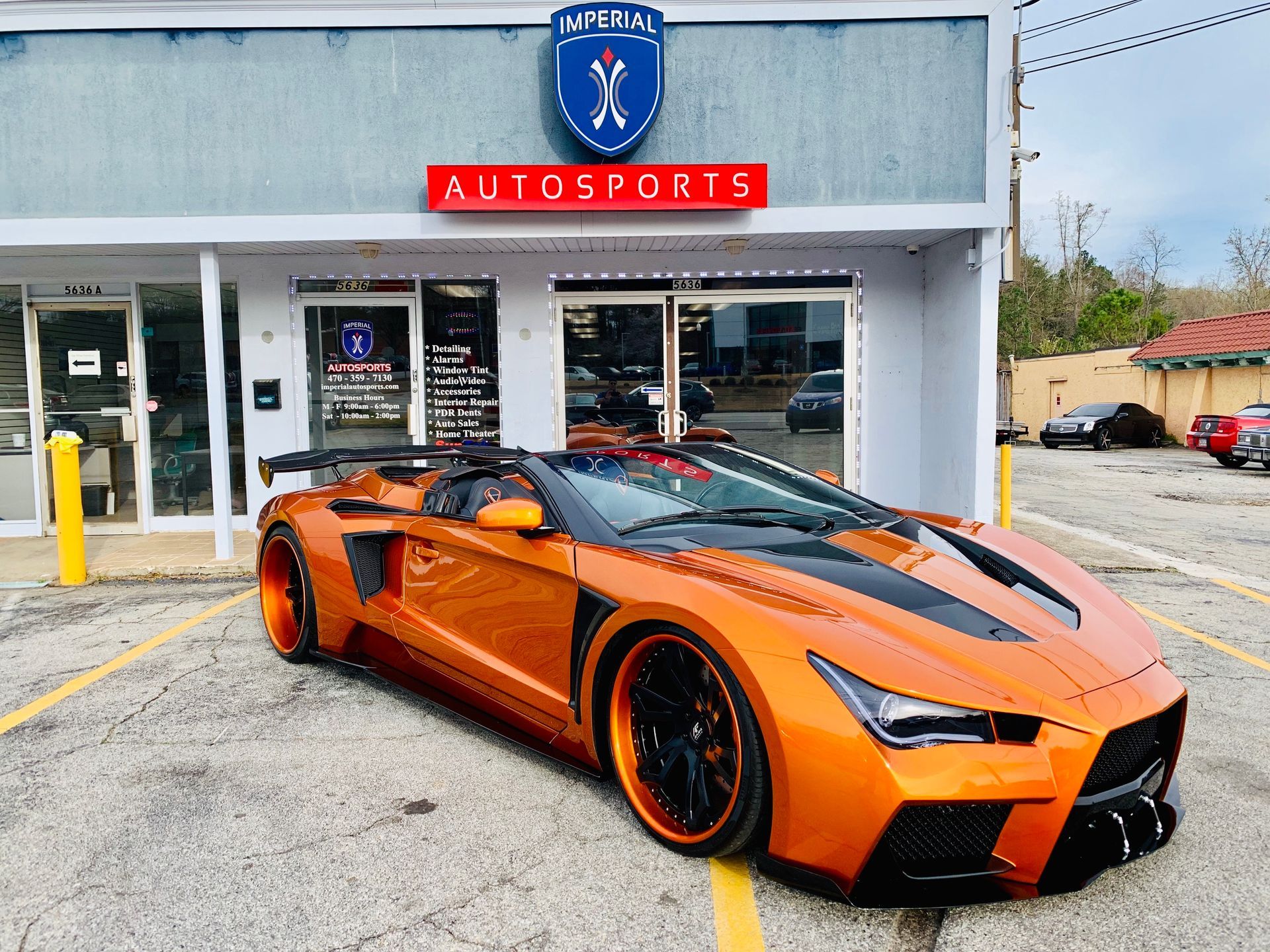An orange sports car is parked in front of a car dealership.