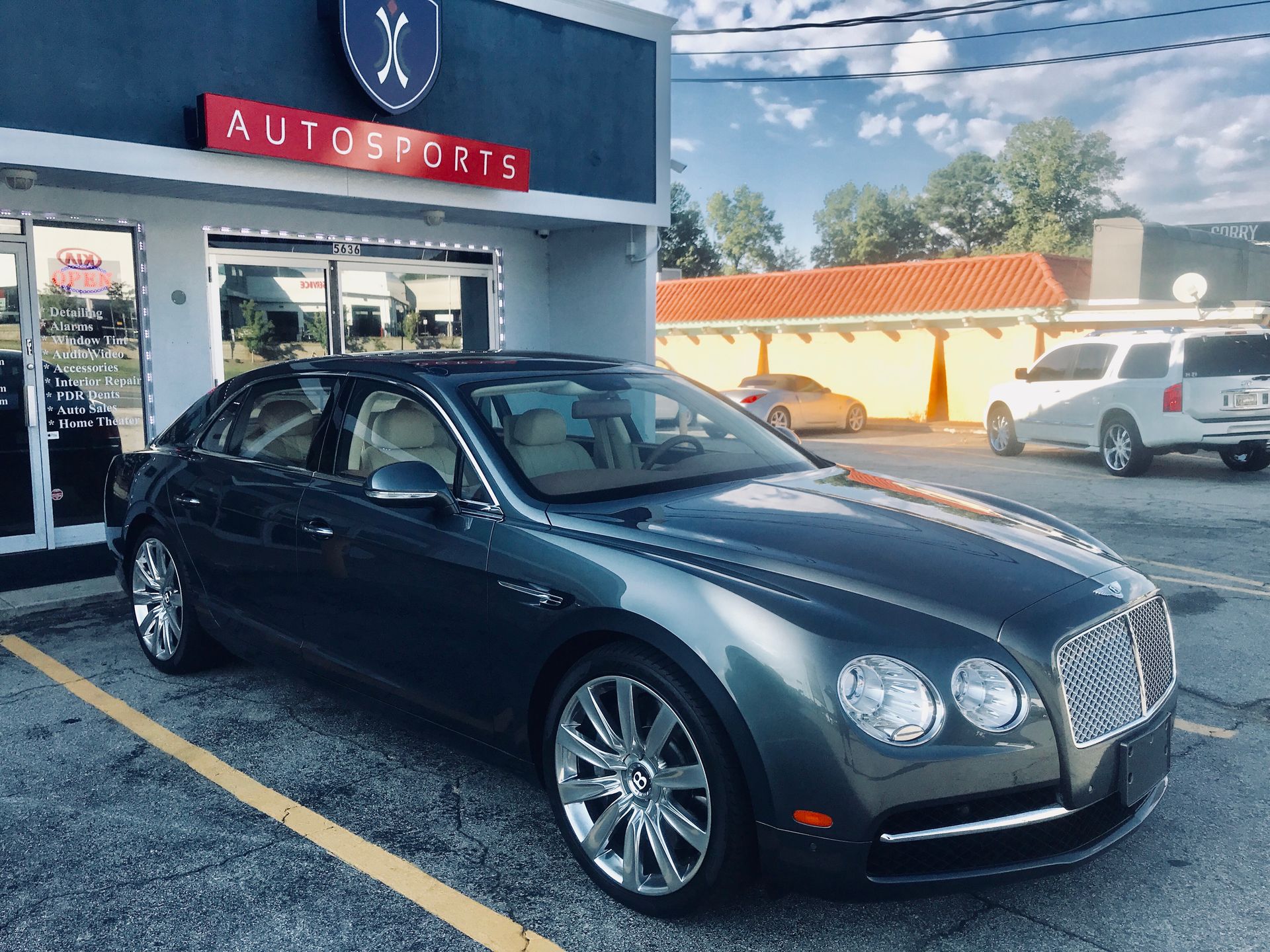 A Bentley Continental Flying Spur is parked in front of a car dealership.