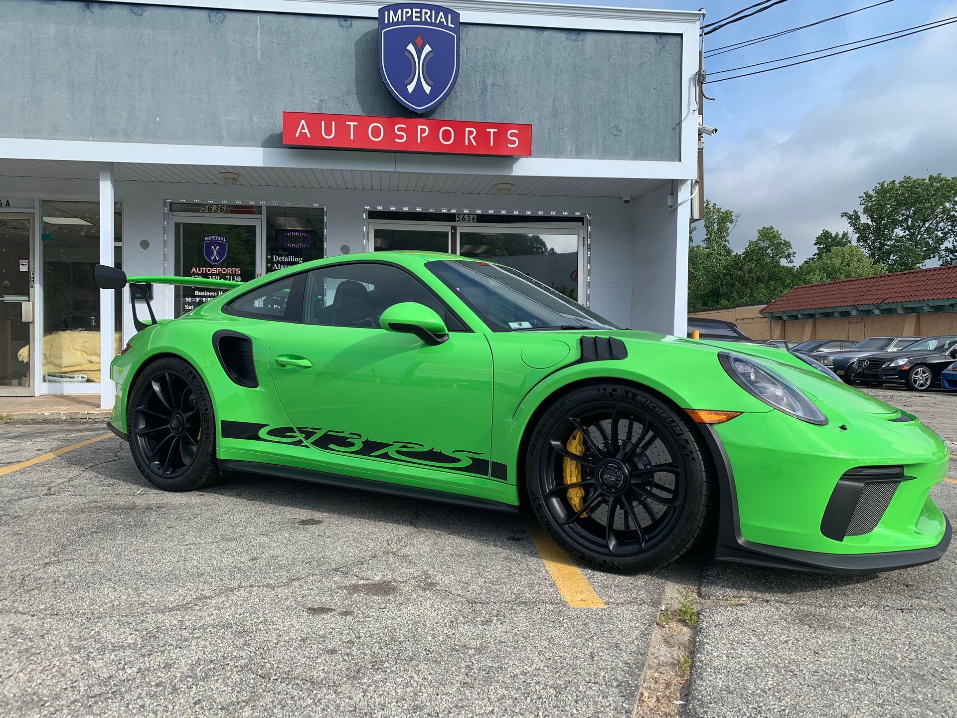 A green Porsche 911 GT3 RS is parked in front of a car dealership.