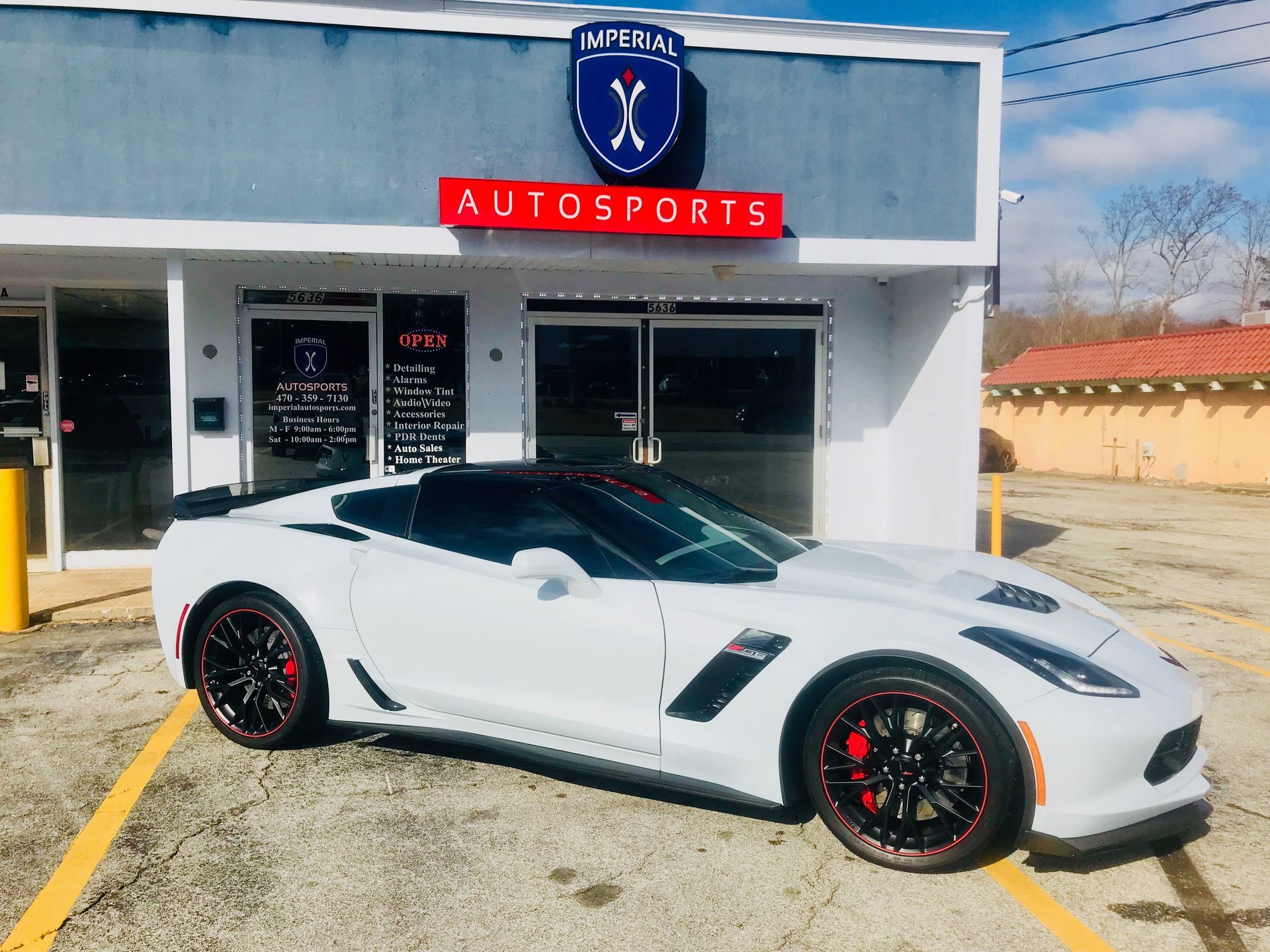 A white sports car is parked in front of a car dealership.