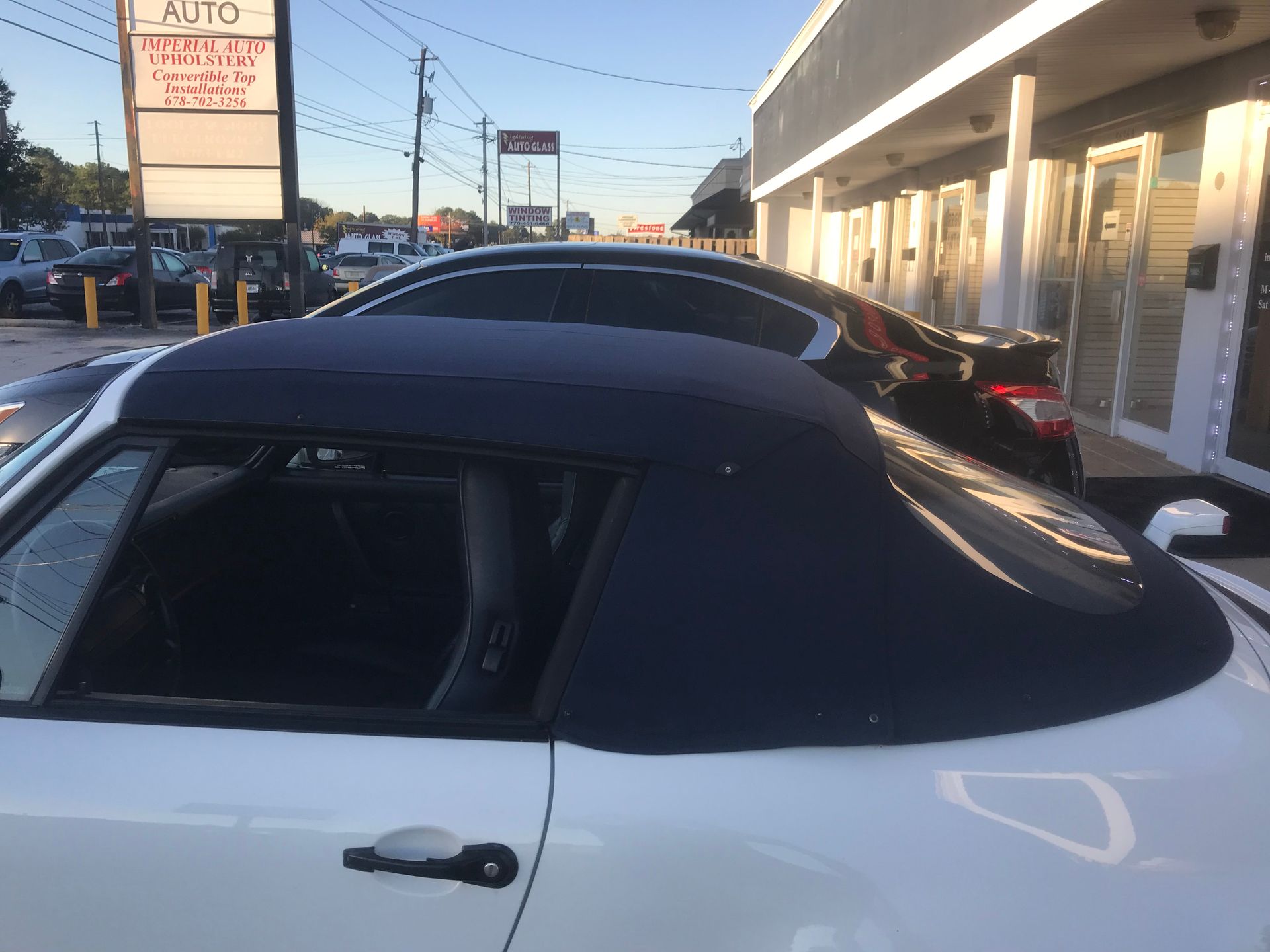 A white convertible with a black top is parked in front of a building.