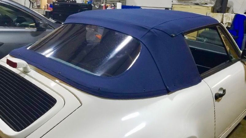 A white convertible with a blue top is parked in a garage.