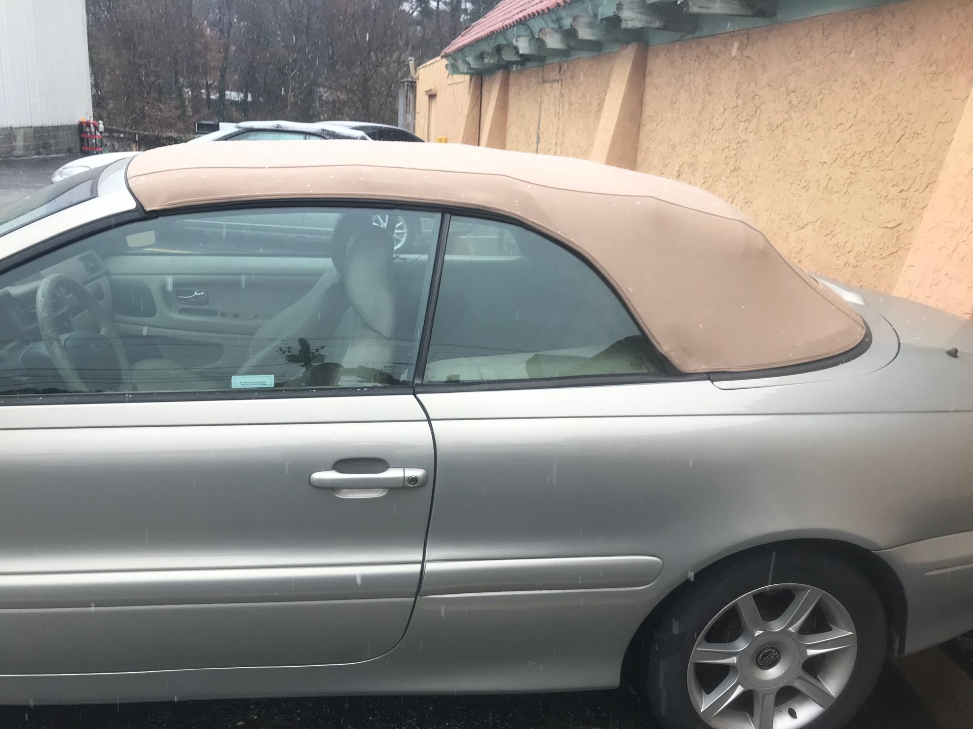 A silver convertible with a tan top is parked in a parking lot