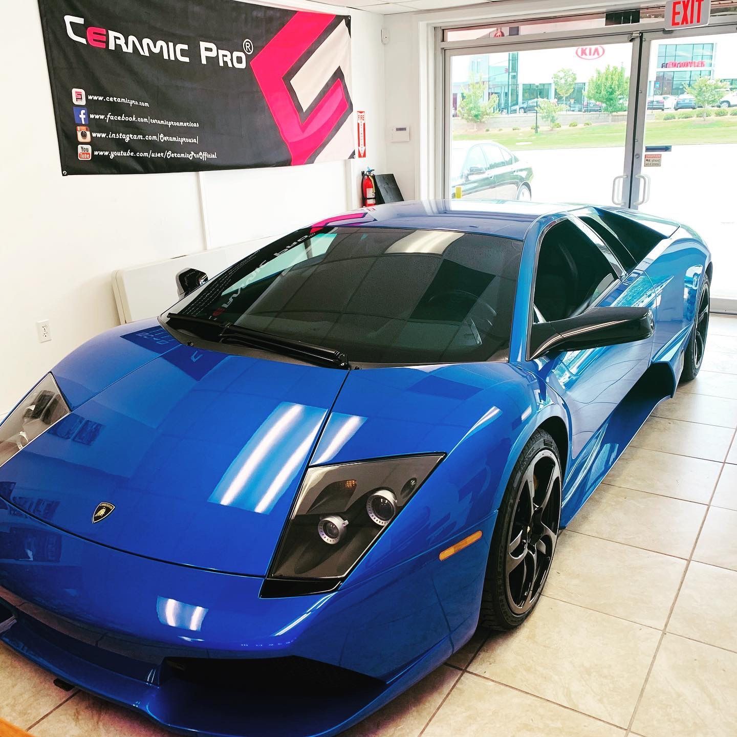 A blue sports car is parked in front of a sign that says ceramic pro