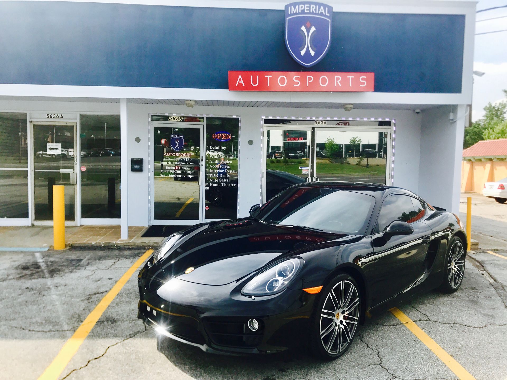 A black sports car is parked in front of an auto sports store
