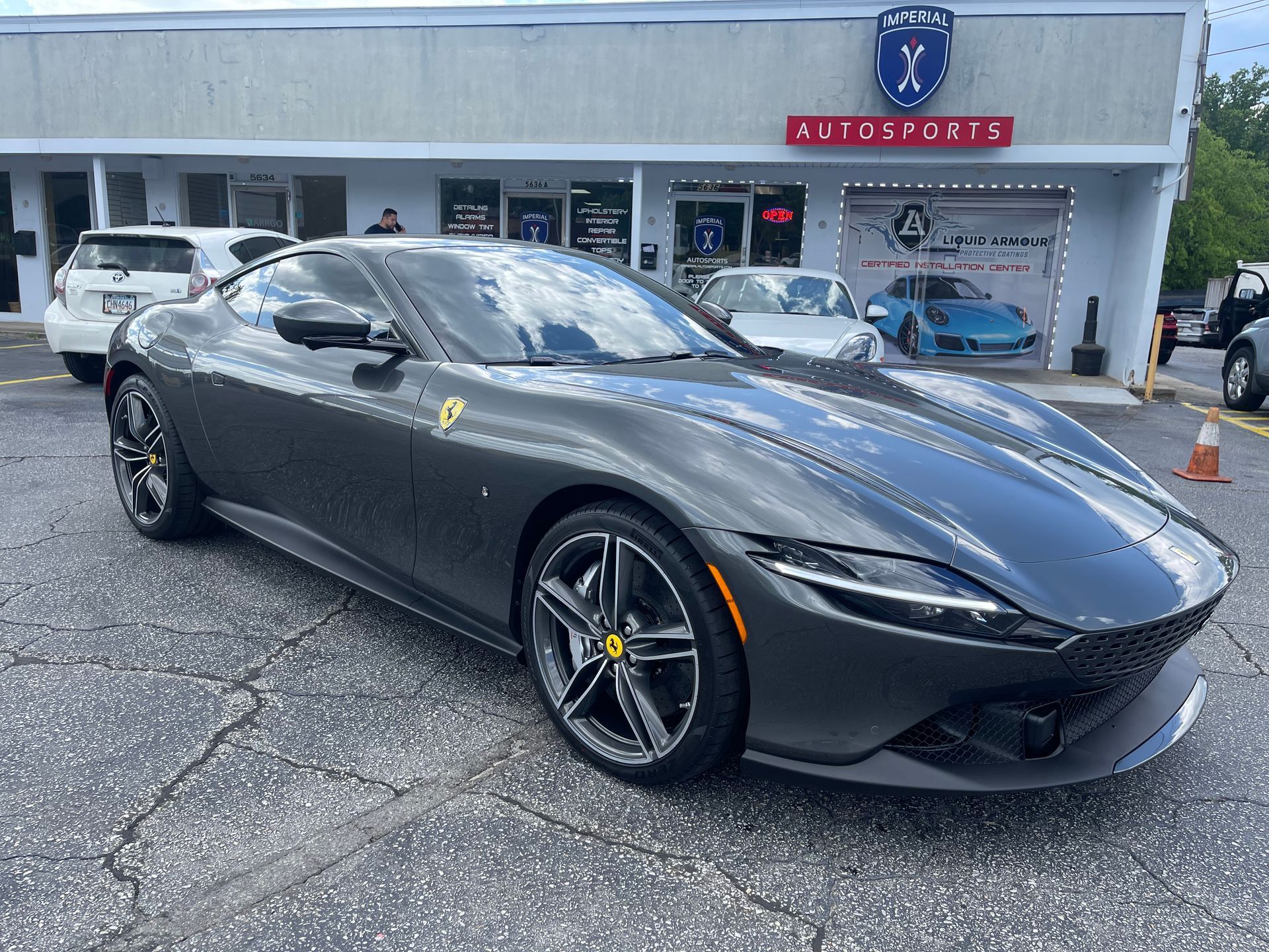 A Ferrari Roma is parked in front of a car dealership.
