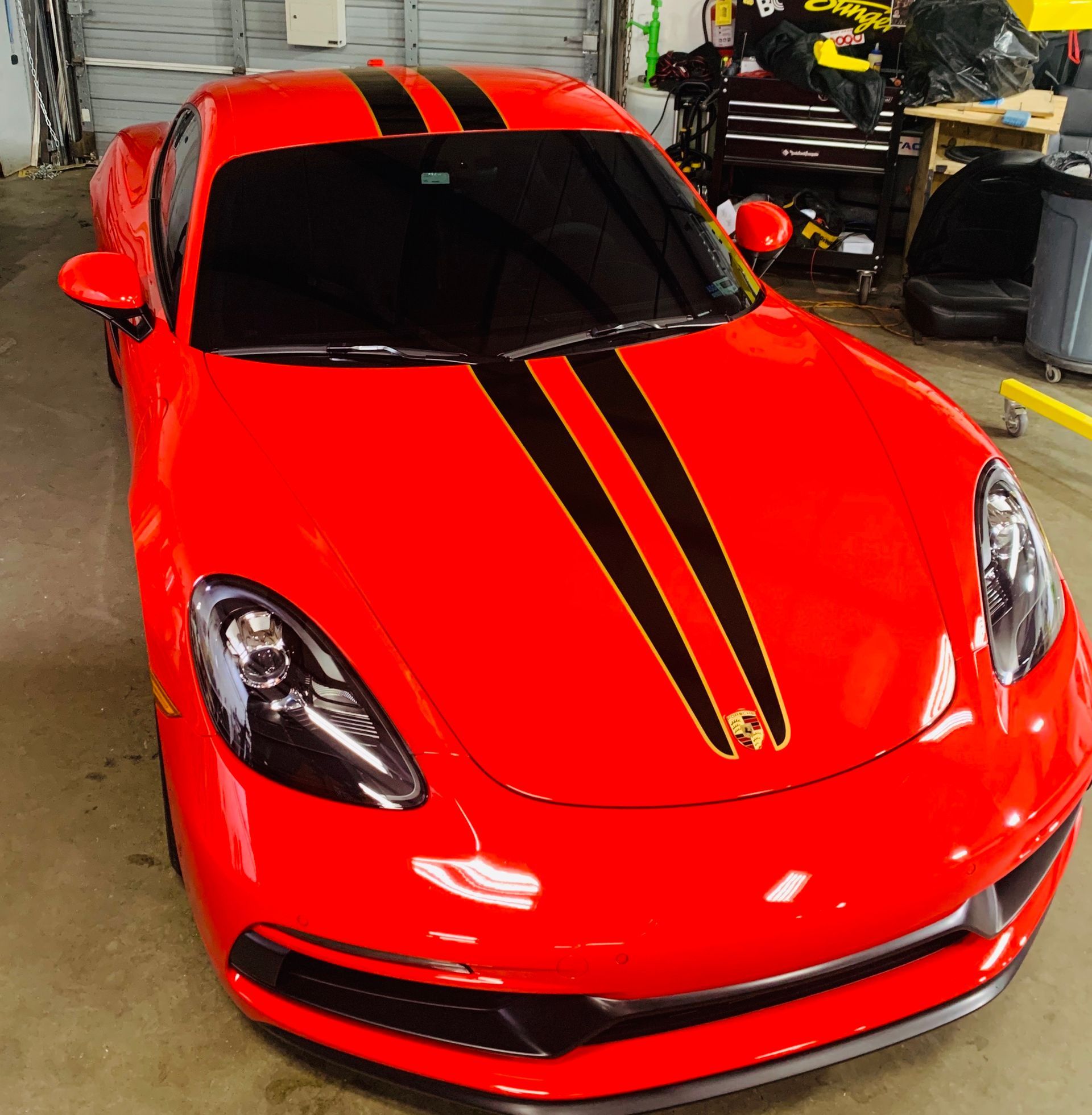 A red sports car with black stripes on the hood is parked in a garage