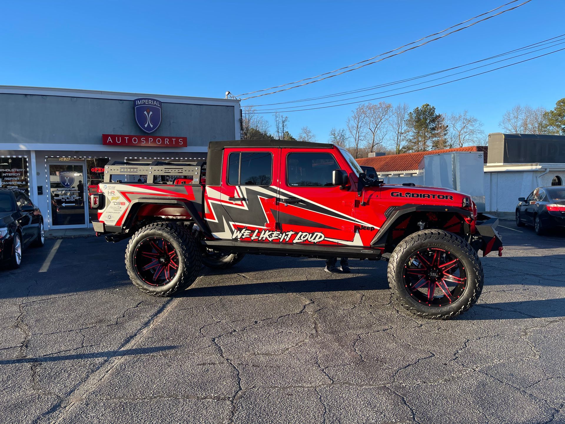 A red Jeep is parked in front of a car dealership.