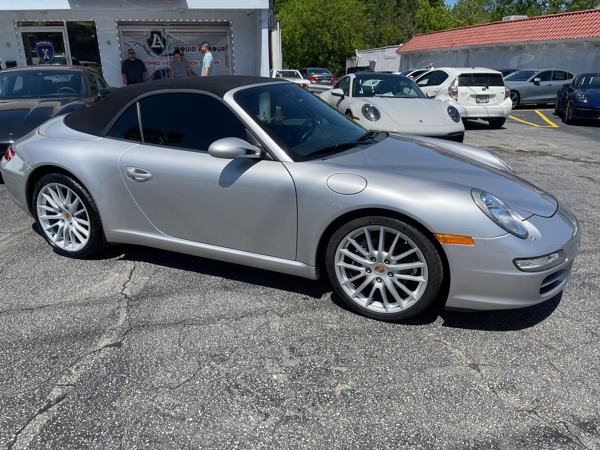 A silver Porsche 911 convertible is parked in a parking lot.