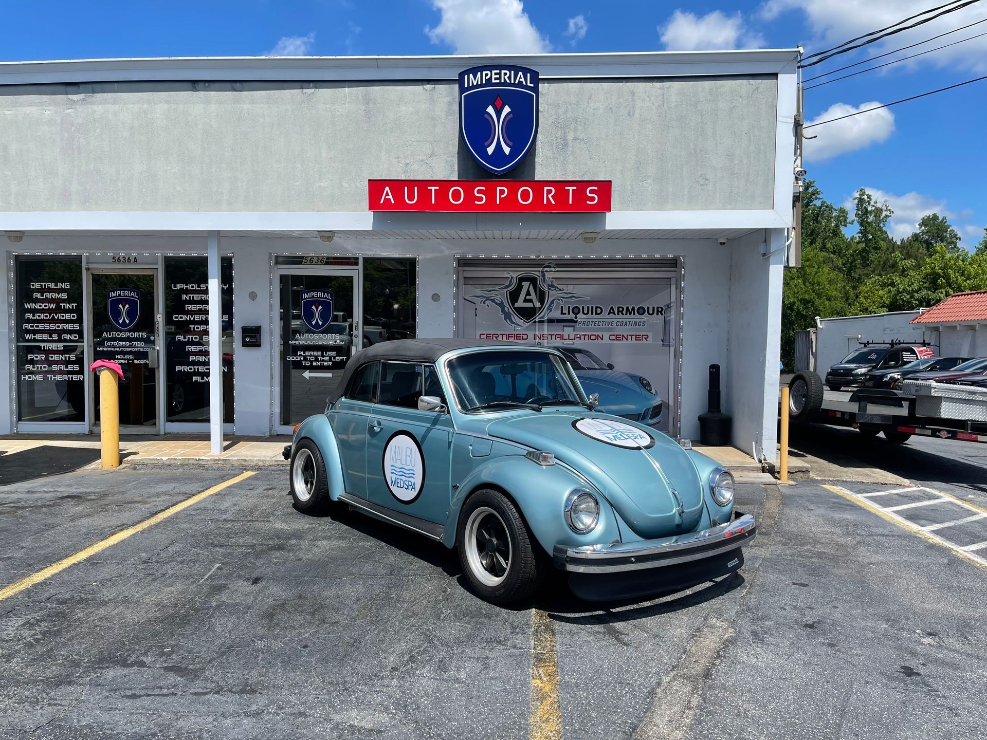 A blue car is parked in front of a car dealership.