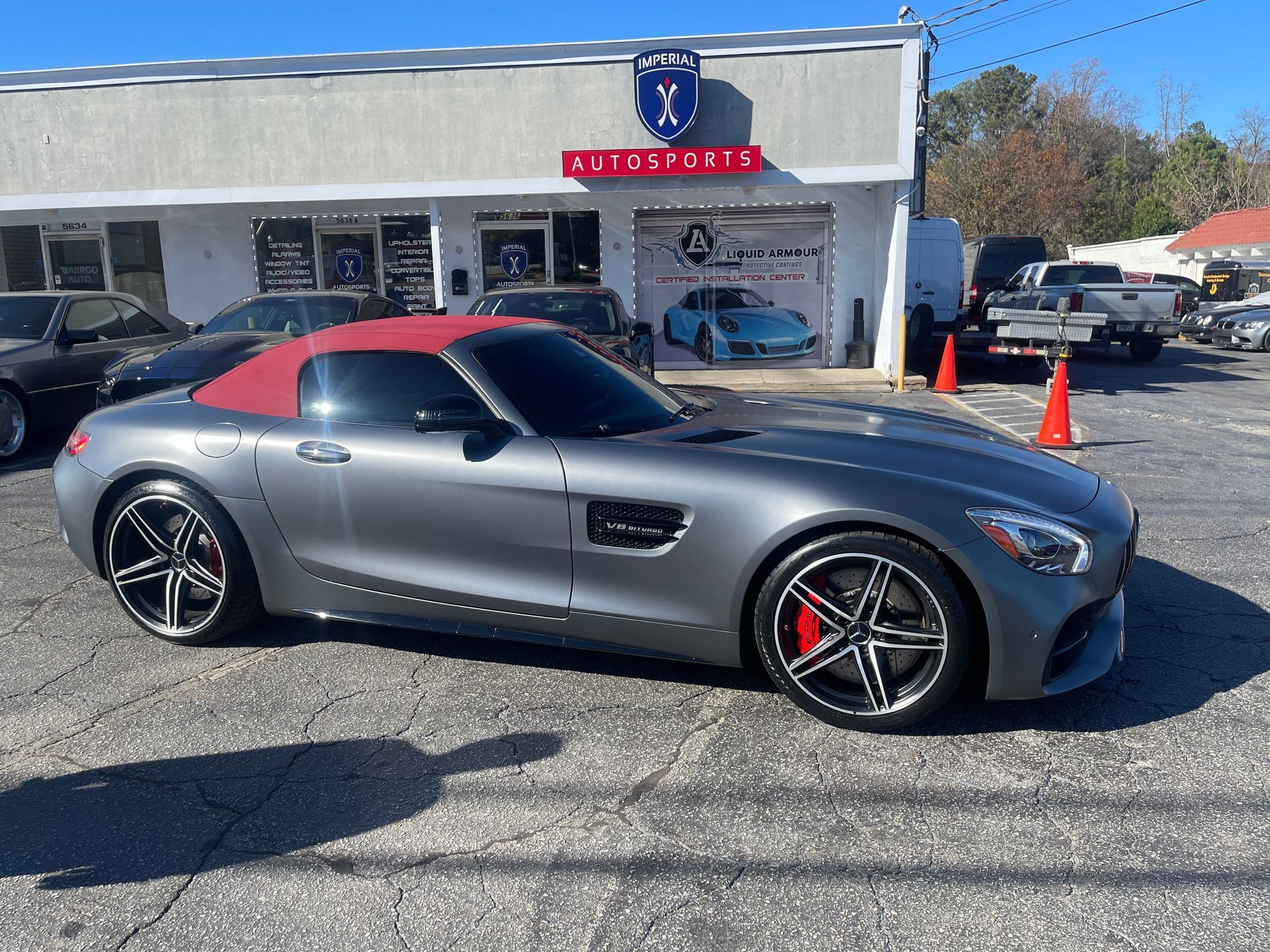 A gray sports car with a red top is parked in front of a building.