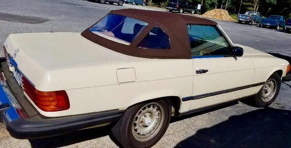 A white convertible car with a brown top is parked on the side of the road.