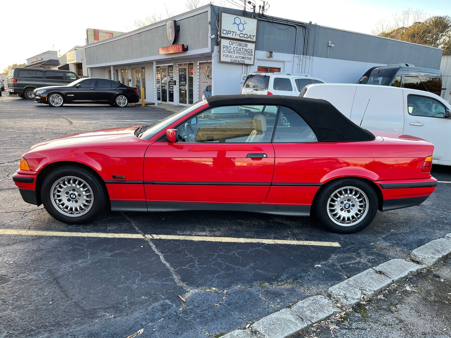 A red convertible is parked in a parking lot in front of a building.