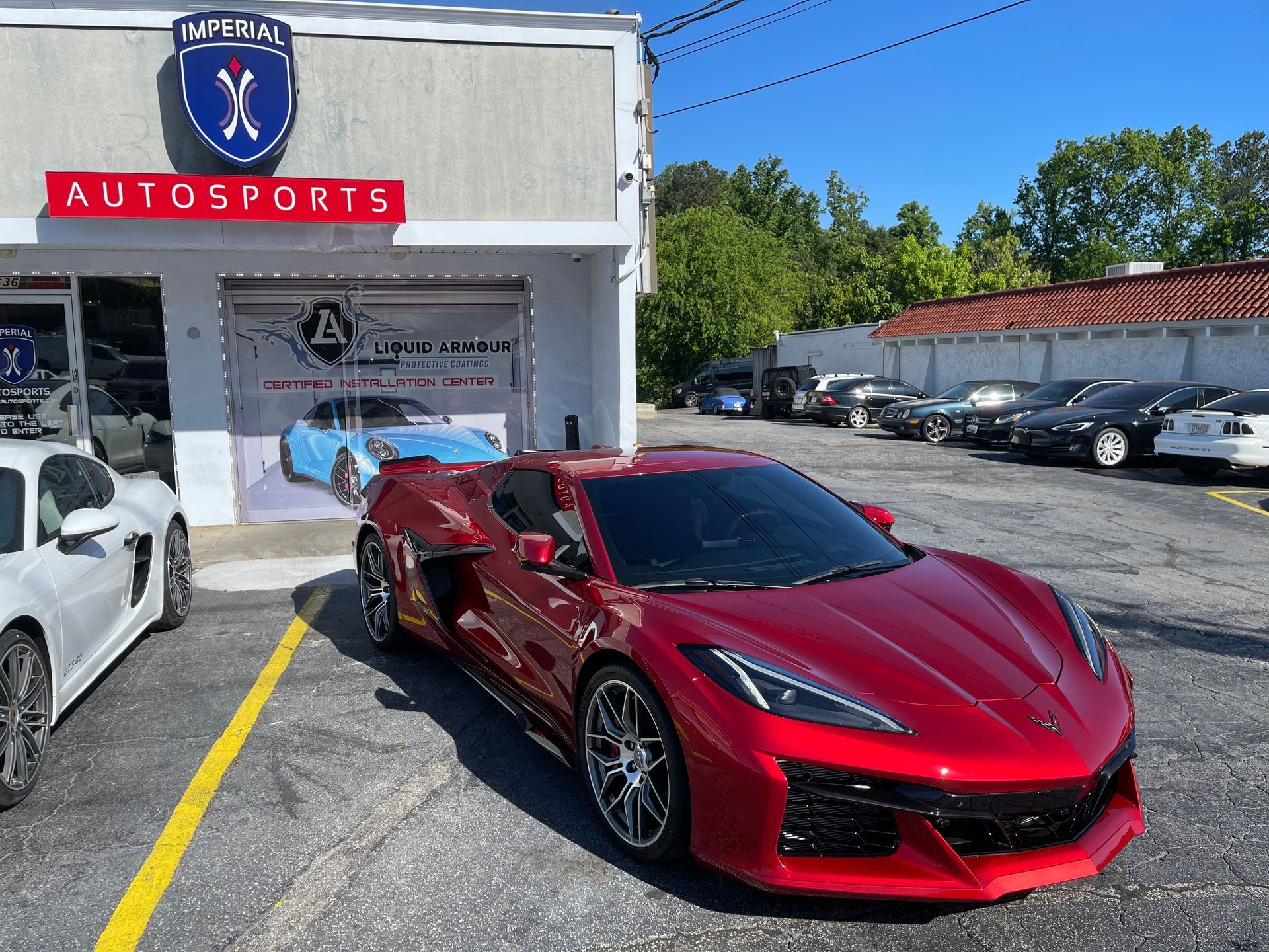 A red Corvette is parked in front of a car dealership.